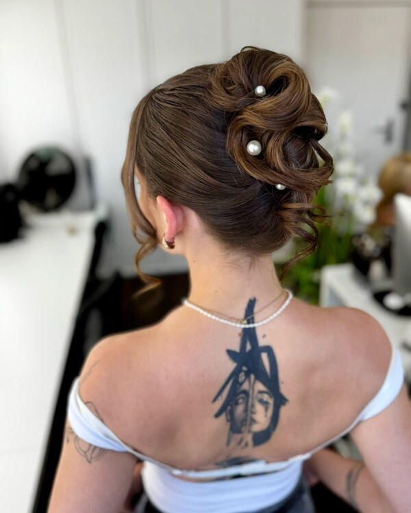 Junge Frau mit Dutt und Perlen im Haar, Rückenansicht, Tattoo am Nacken